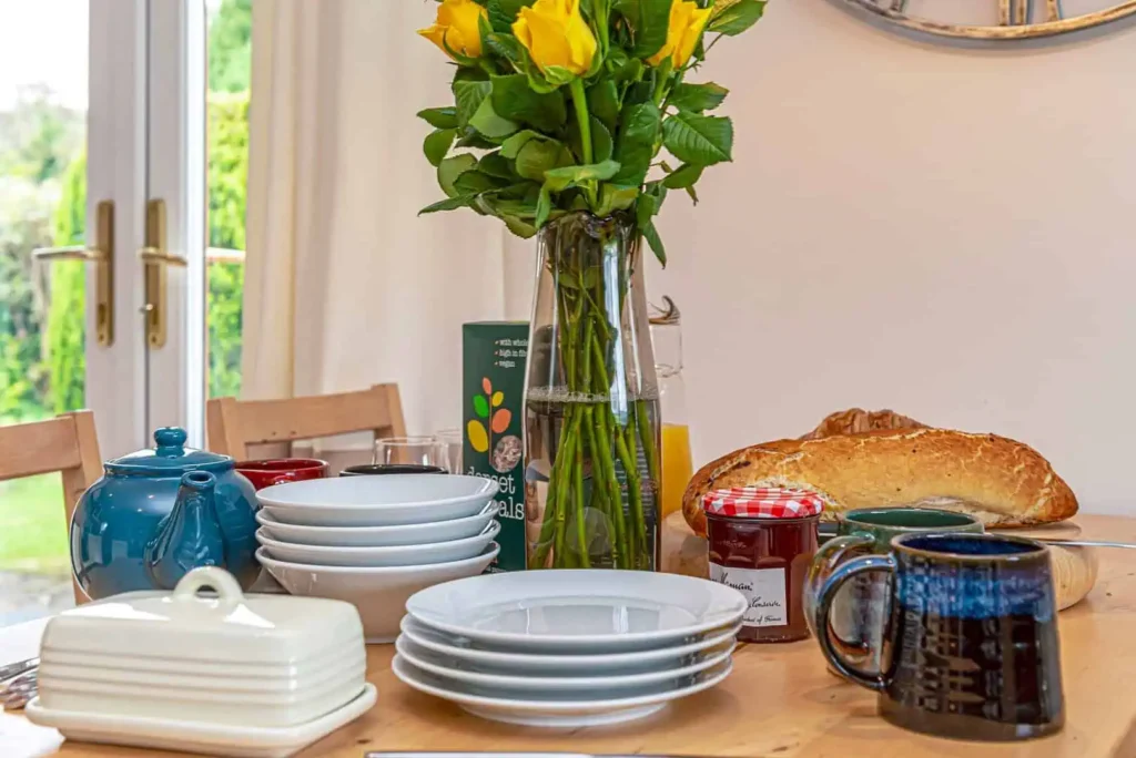 A close-up of a dining table set for a delicious breakfast with fresh bread, jam and a vase of yellow roses