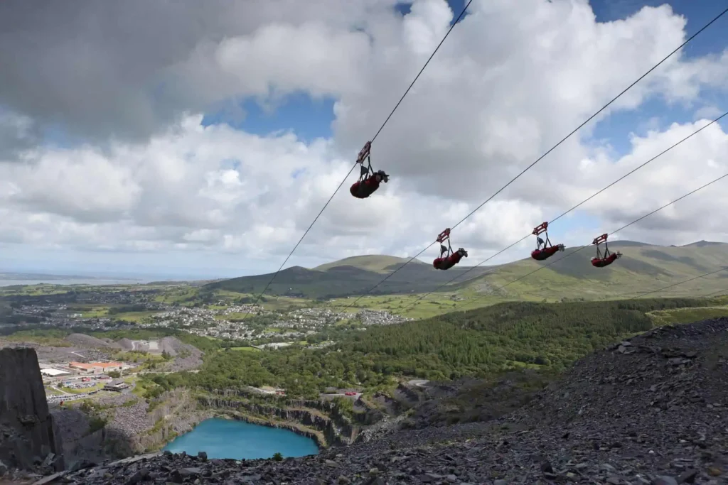 Four people riding side-by-side on the Zip World Velocity zip line over the Penrhyn slate quarry
