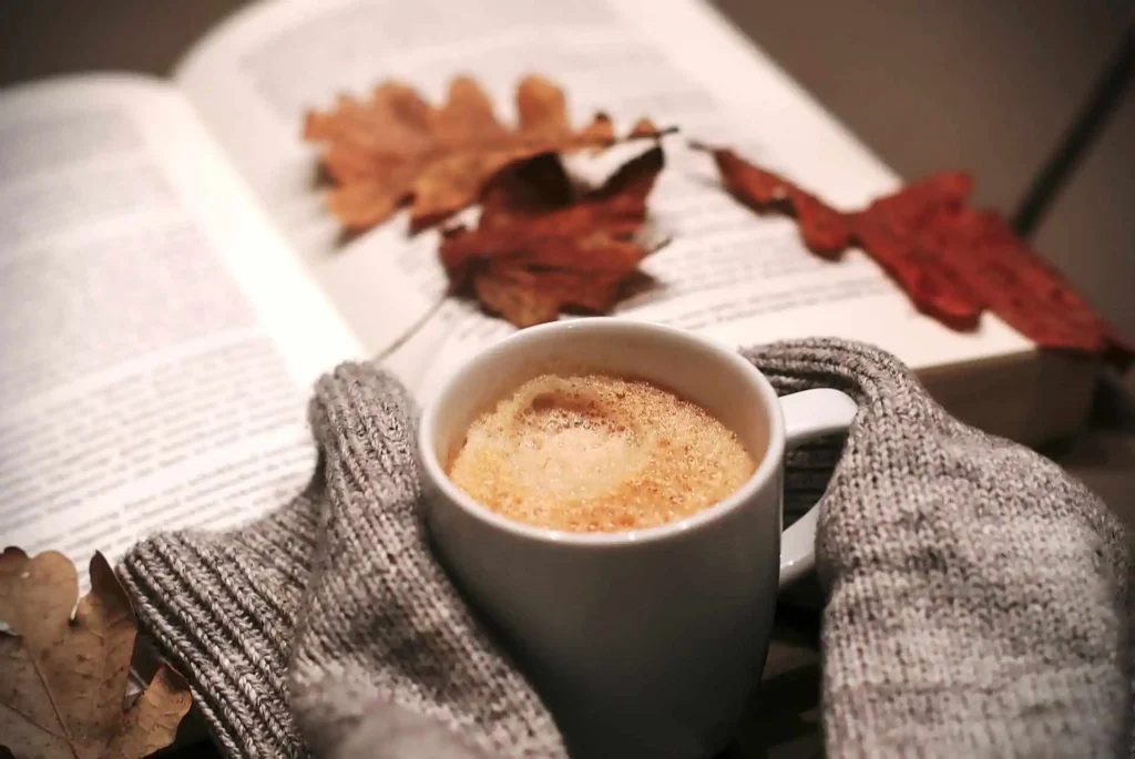 cottage vs hotel: coffee mug and open book on a table with autumn leaves around in the privacy of your cottage