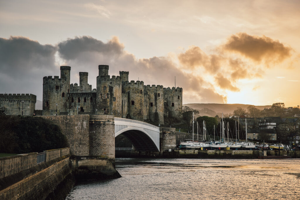 Conwy Valley Getaway | conwy castle early evening Golden sunset light illuminates Conwy Castle and its eight towers, with warm colours reflecting in the calm waters of the estuary in front of the historic bridge