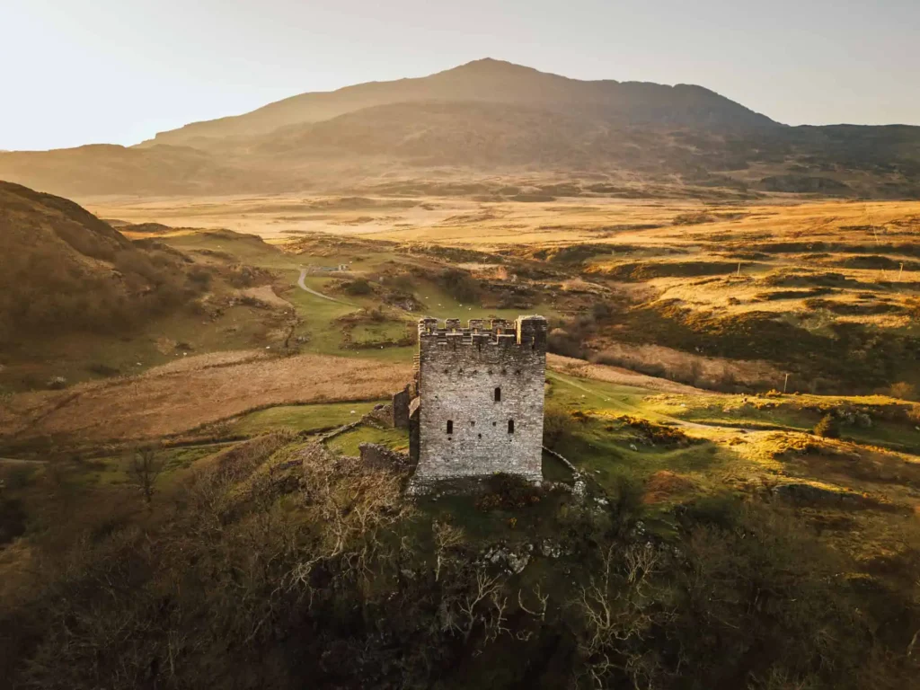 Conwy Valley Getaway | dolwyddelan castle The stone keep of Dolwyddelan Castle standing alone on a rocky hill, with the dramatic mountains of Eryri (Snowdonia) rising behind it under a cloudy sky.