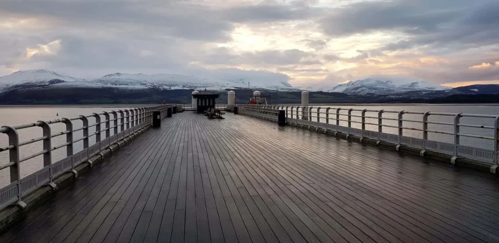 Conwy Valley Getaway | 41361 beaumaris pier menai strait web optimised 1920px The wooden decking of Beaumaris Pier leading out over the calm waters of the Menai Strait, with traditional Victorian lampposts lining the walkway