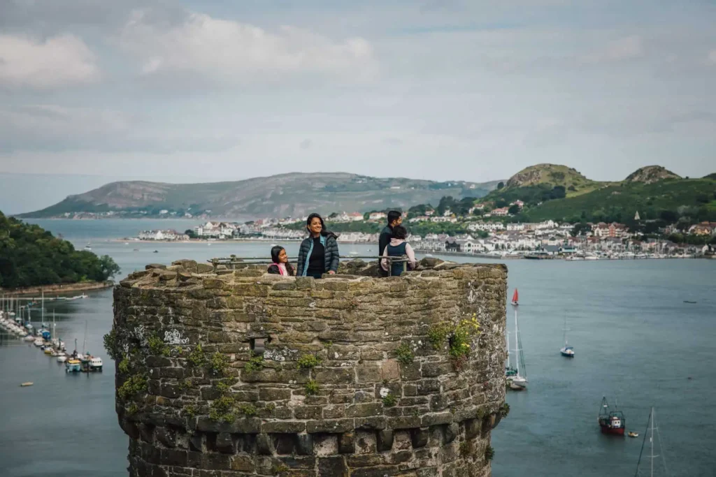 Visitors looking out from the stone battlements on top of a tower at Conwy Castle, enjoying the panoramic view over the town and the Conwy Estuary