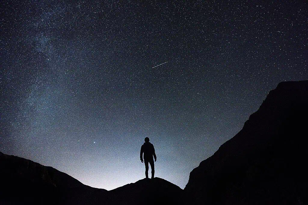 Stargazing in Snowdonia with a man standing on a mountain looking up at the night sky full of stars