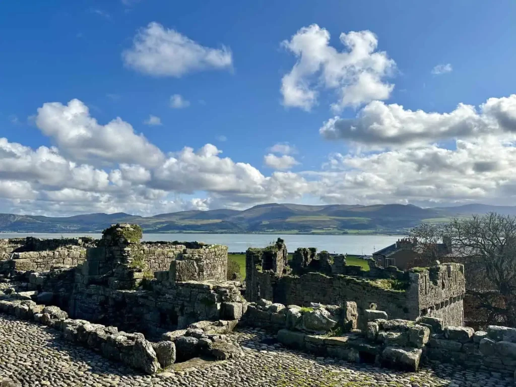 Conwy Valley Getaway | 733655 svw h12 2526 0002 Ruins of Beaumaris Castle with the calm waters of the Menai Strait in the background, framed by distant hills under a soft sky