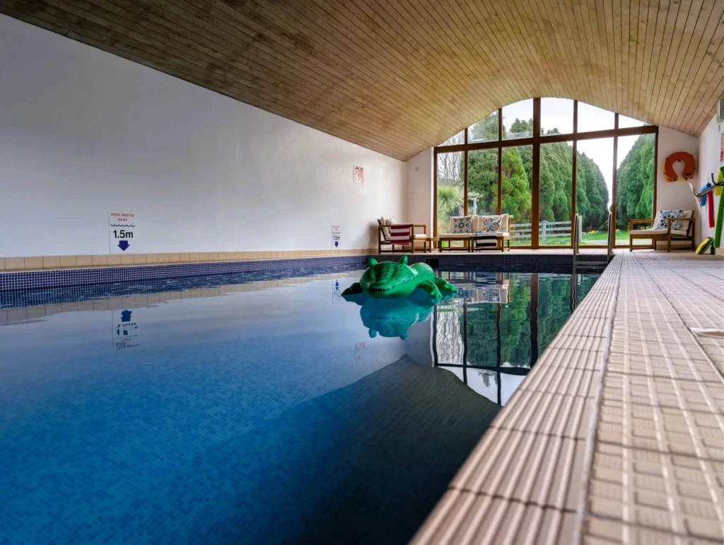 Panoramic view of the indoor heated swimming pool at Conwy Valley Getaway, featuring large windows with views toward the garden