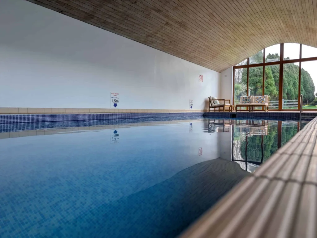 Conwy Valley Getaway | new indoor pool floor level View across the still water of the indoor swimming pool toward the seating area and large glass windows.