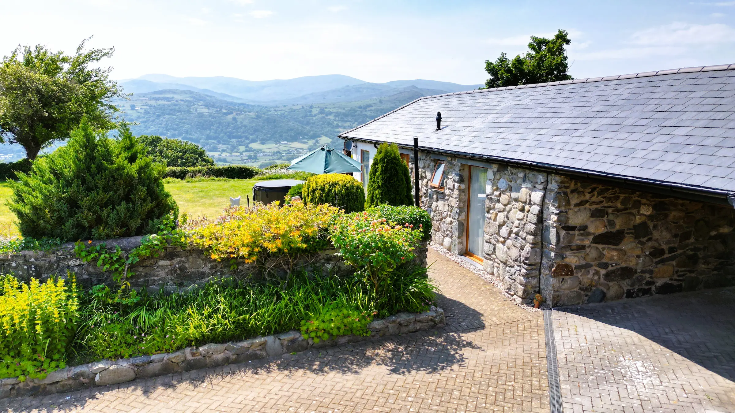 View showing the stone side of Fig Tree cottage with garden on the left side and mountains in the background