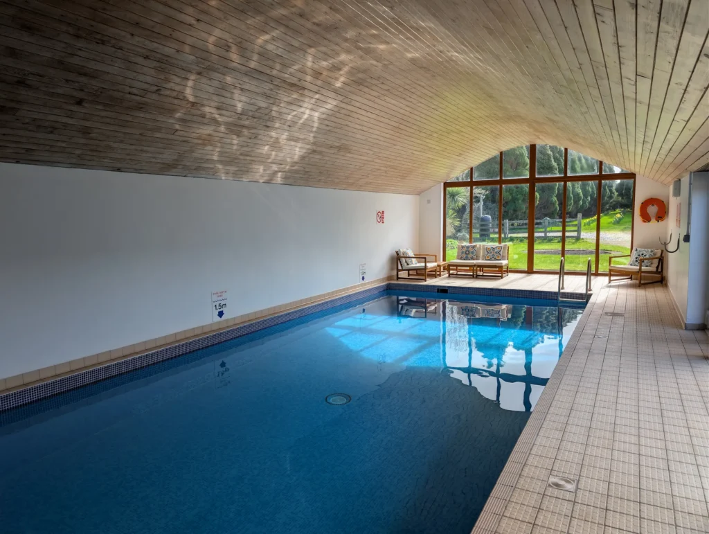 The indoor swimming pool at Conwy Valley Getaway with sunlight reflecting off the water and the garden highlighted through the end glass windows