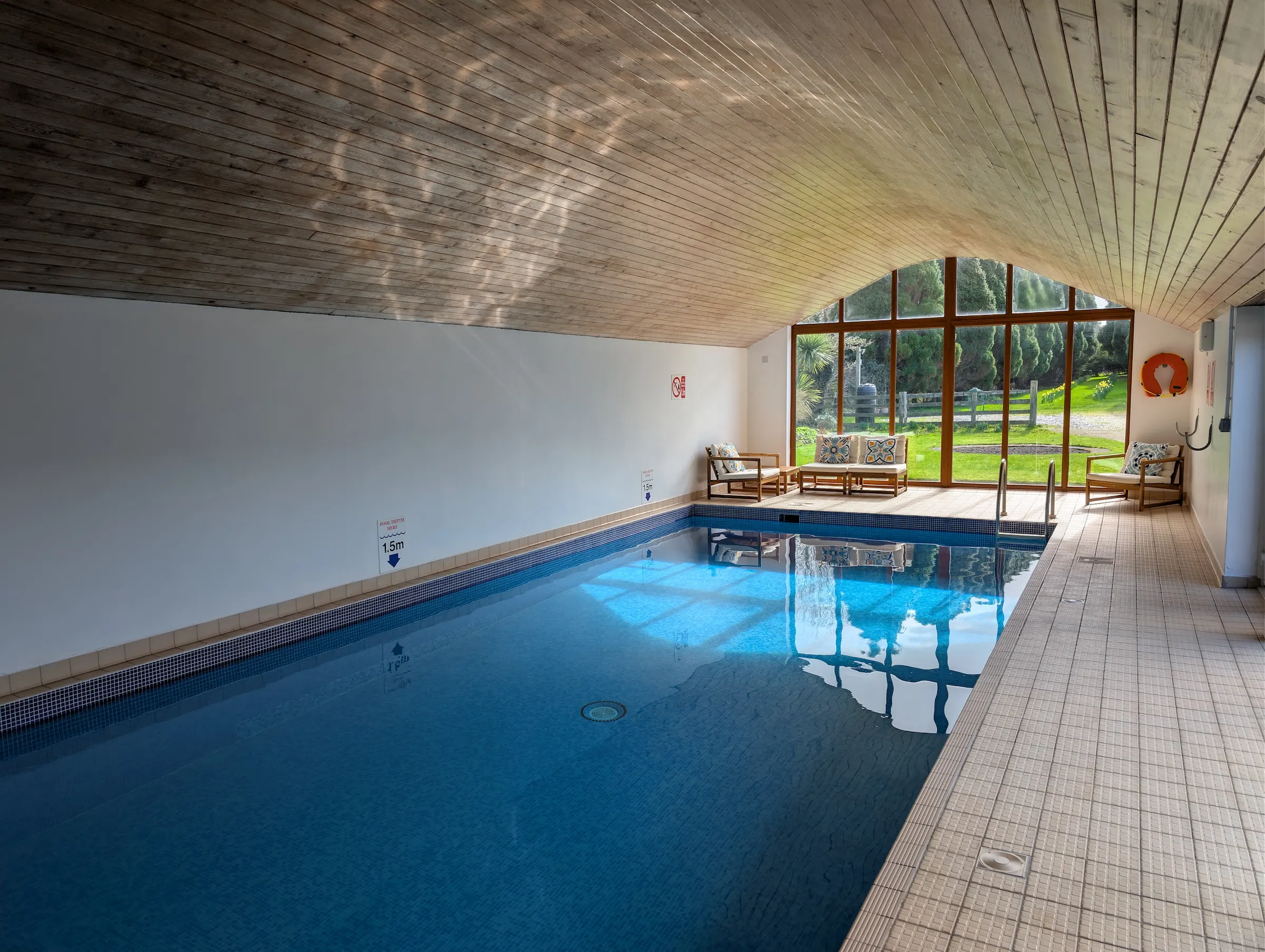 The indoor swimming pool at Conwy Valley Getaway with sunlight reflecting off the water and the garden highlighted through the end glass windows