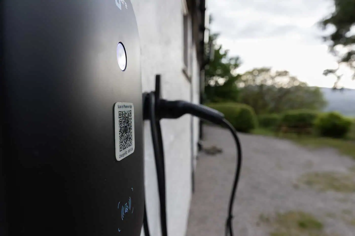 Close-up of EV charging point QR code and cable at Conwy Valley Getaway with garden in background