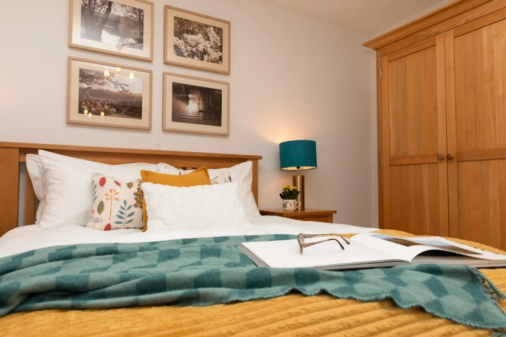 Fig Tree master bedroom with gallery prints, teal lamp, open book and glasses, low angle