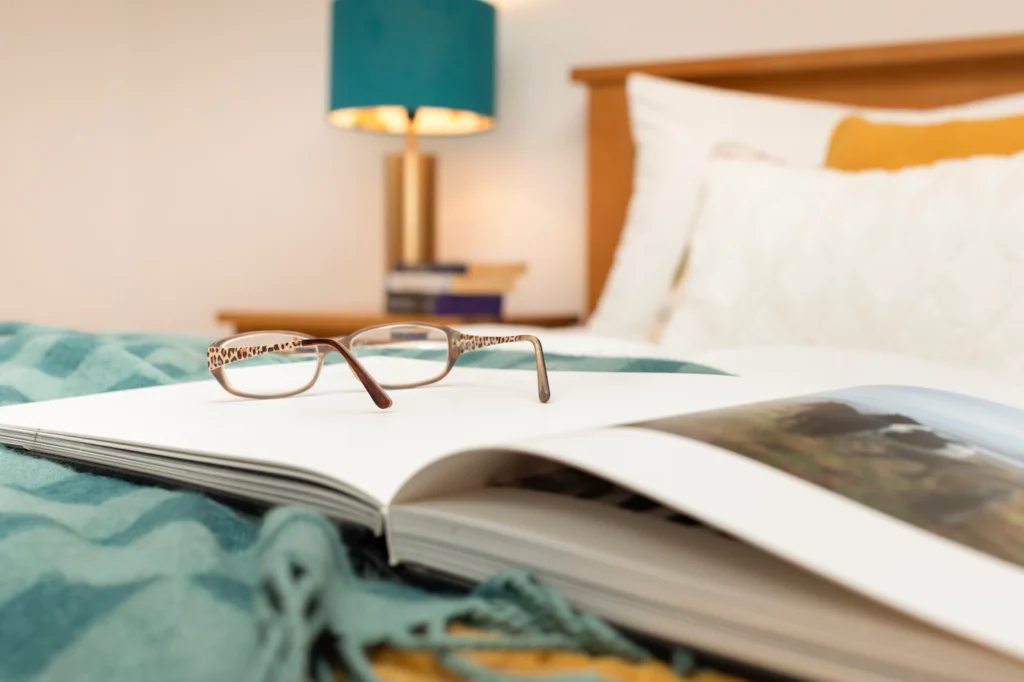 Glasses resting on open book beside teal lamp in Fig Tree cottage bedroom